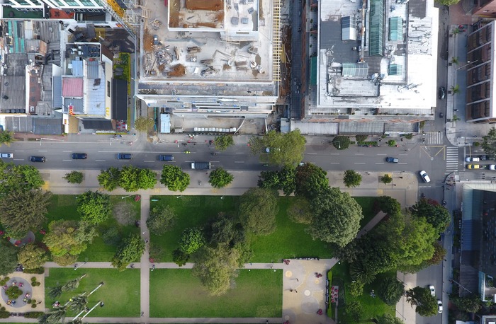 Vista aérea de una zona urbana. Una calle divide la foto a la mitad en horitzontal. La parte superior muestra los terrados de tres edificios. La parte inferior muestra una zona verde planificada, con césped y árboles
