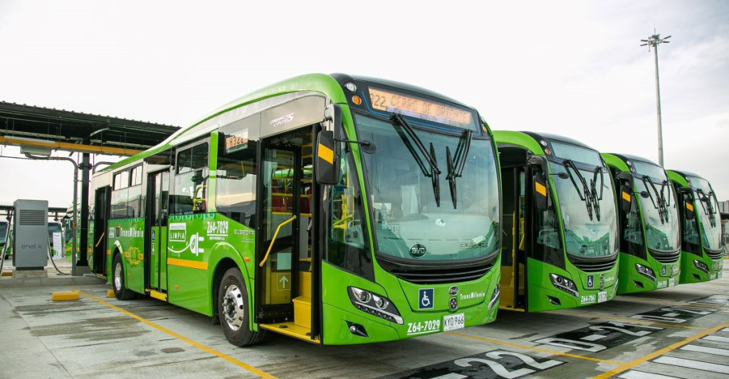 Un grupo de cuatro autobuses están orientados hacia la derecha. Son de color verde y paracen parte de una flota a estrenar. Se lee "energía eléctrica limpia"
