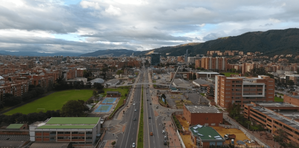 Imagen aérea de la ciudad de Bogotá de día. Al centro se ve una avenida, a la izquierda una zona verde. A la derecha y al fondo se pierde la vista en innumerables edificios de ladrillo rojo.